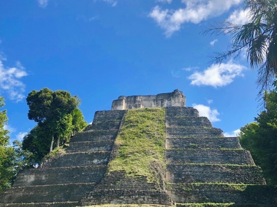 Une vaste pyramide antique à sommet plat, entourée d’une végétation luxuriante et surplombée d’un ciel bleu clair.