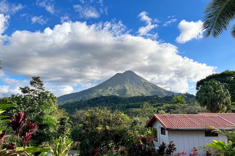 A lush green landscape with a prominent mountain and a small white building with a red roof.
