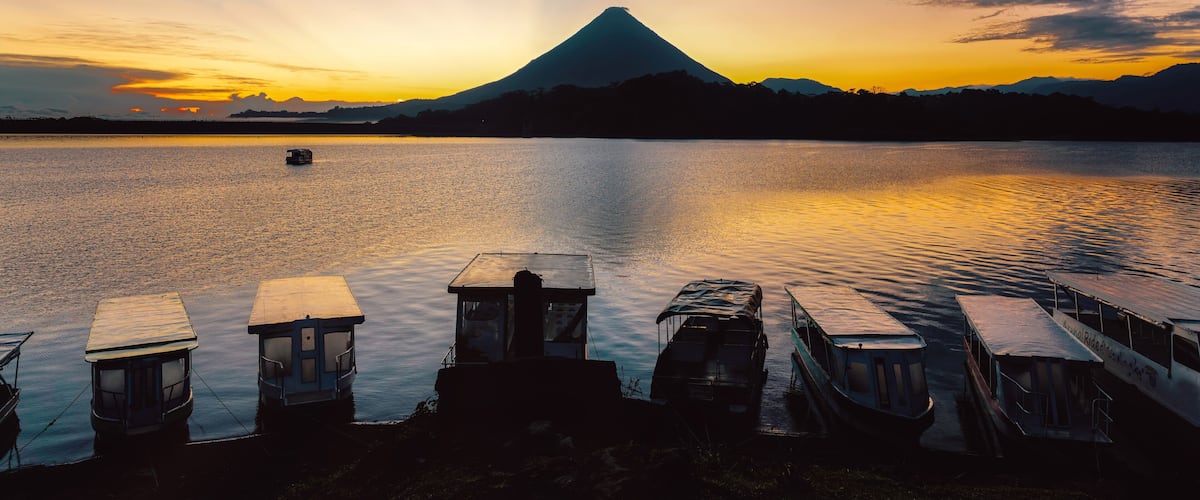 A sunset over a calm lake with a boat dock, a mountain in the background, and a clear sky.