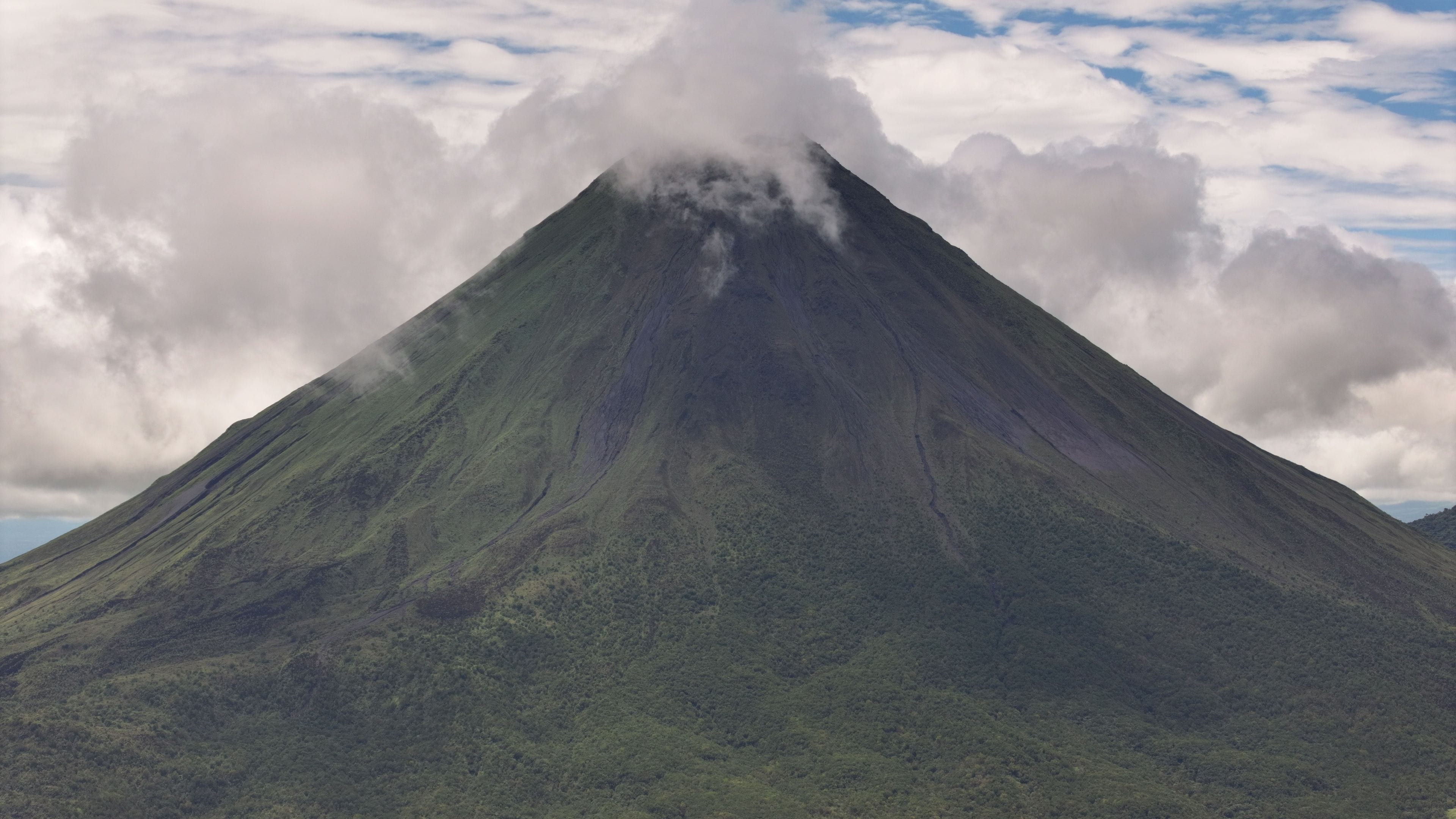 Aerial view of Arenal Volcano with clouds around its peak and lush green slopes, San Carlos, Alajuela Province, Costa Rica.
