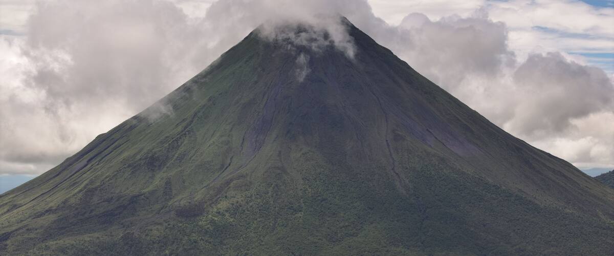 Aerial view of Arenal Volcano with clouds around its peak and lush green slopes, San Carlos, Alajuela Province, Costa Rica.