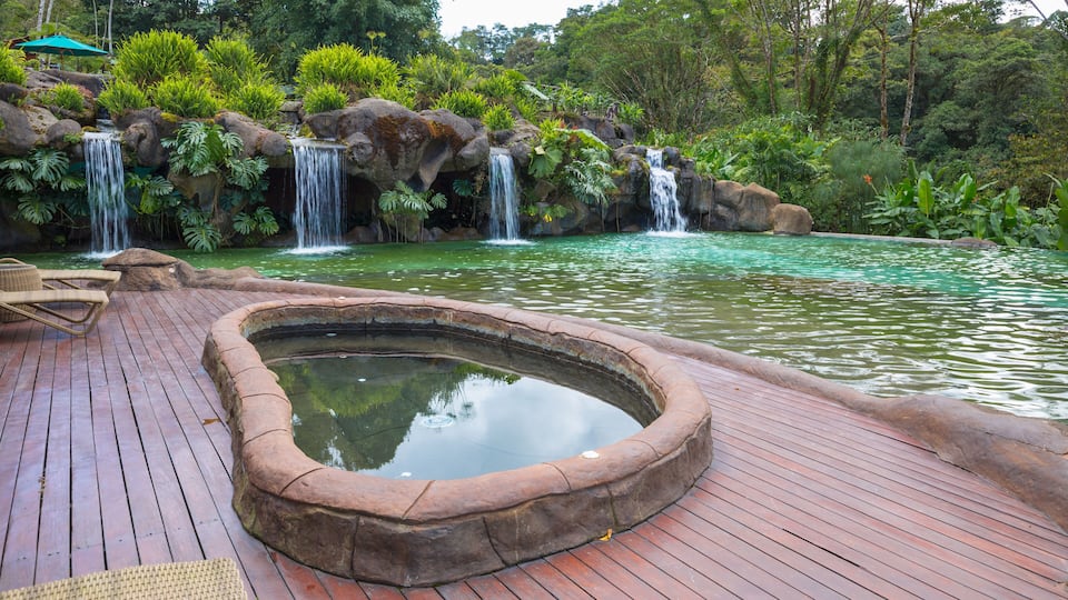 A wooden deck with a small pond and three waterfalls in a lush garden.