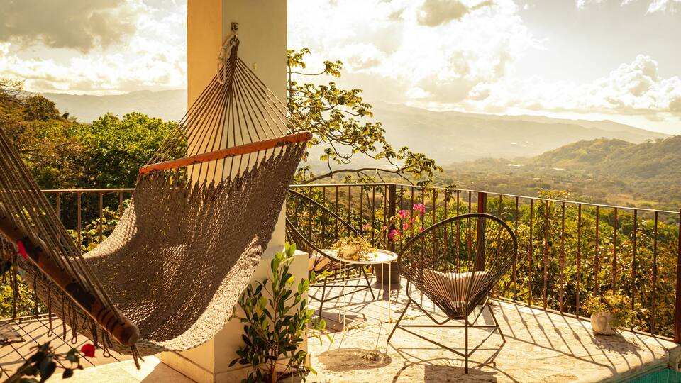 A hammock, chairs, a pool, and a scenic view of mountains and greenery.