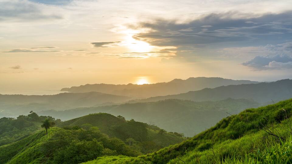 A sunrise over a mountainous landscape with lush greenery.