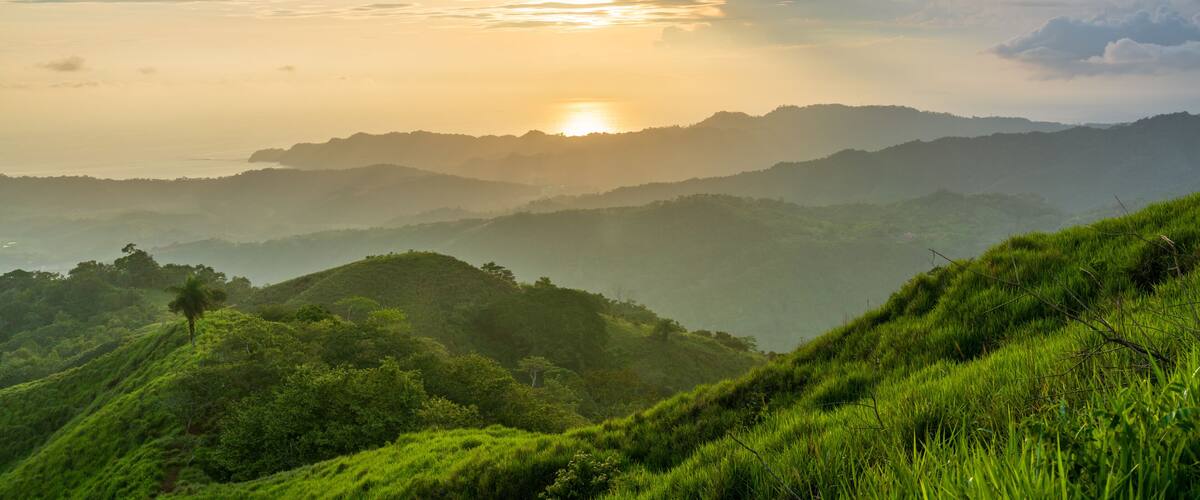 A sunrise over a mountainous landscape with lush greenery.