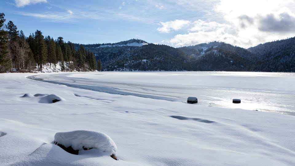 A snow-covered lake with mountains in the background and a clear sky.