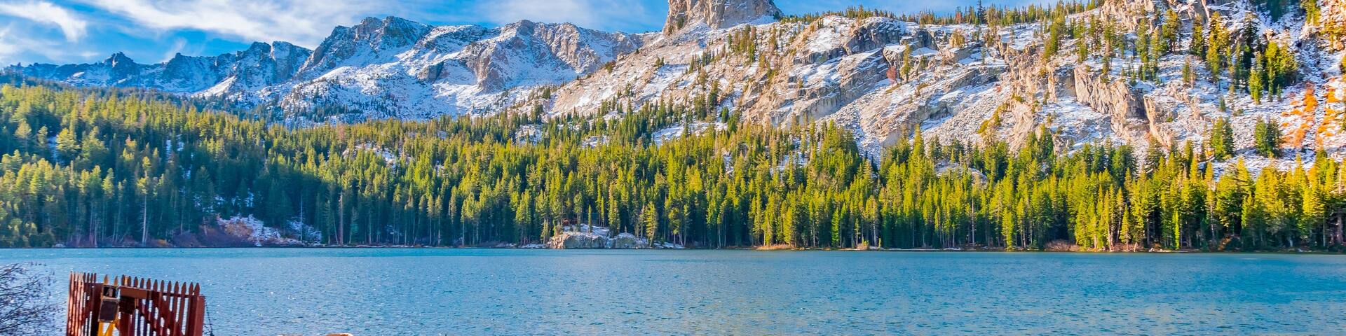 A lake with wooden boats docked on a pier, surrounded by snow-capped mountains and dense forests.