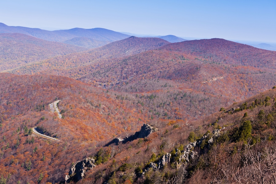 A mountainous landscape with autumn foliage, a winding road, and a clear sky.