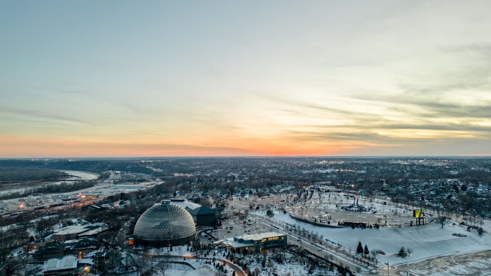 A cityscape at dusk with a large dome-shaped building, snow-covered streets, and a river in the background.