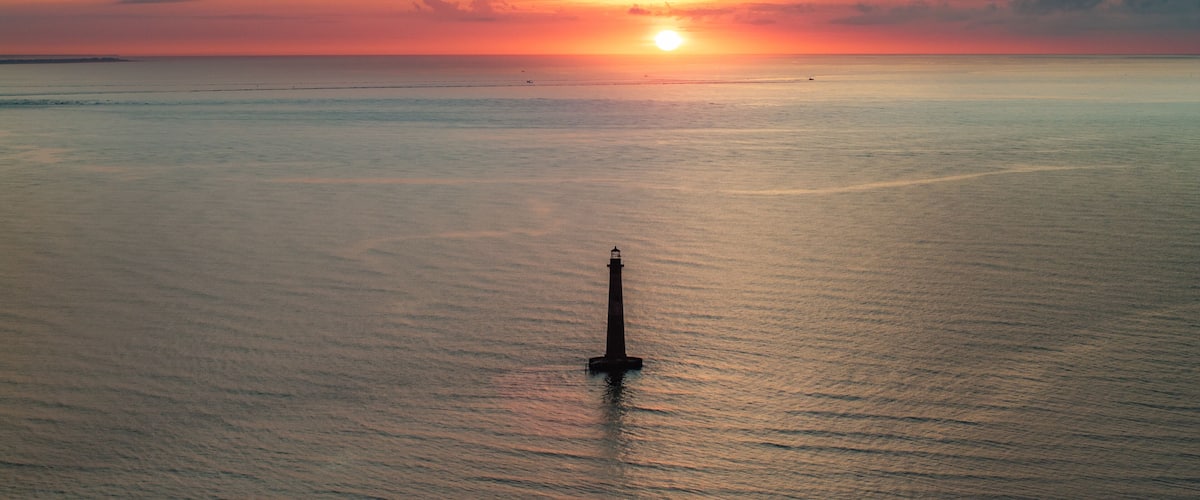 A lighthouse at sea during sunset.