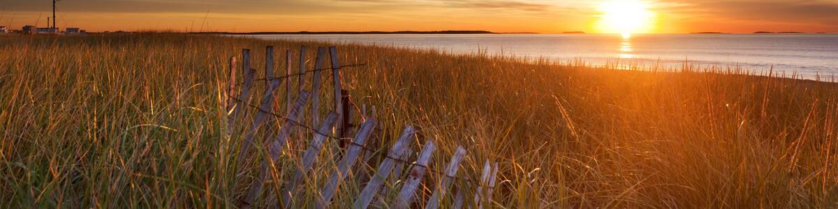 A sunset over a grassy field with a fence in the foreground.