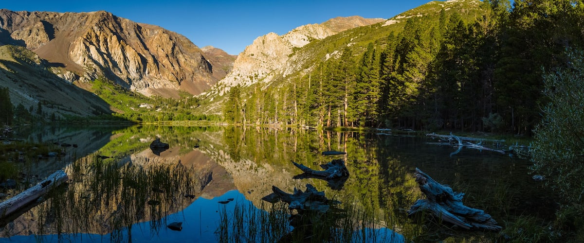 A mountain lake with reflections, surrounded by forest and rocky cliffs.