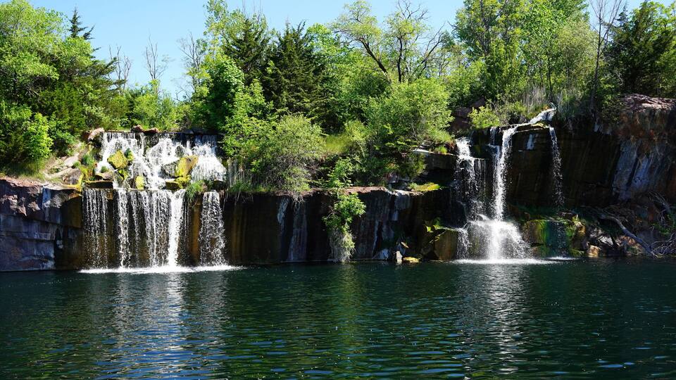A waterfall cascading into a clear lake surrounded by dense forest.