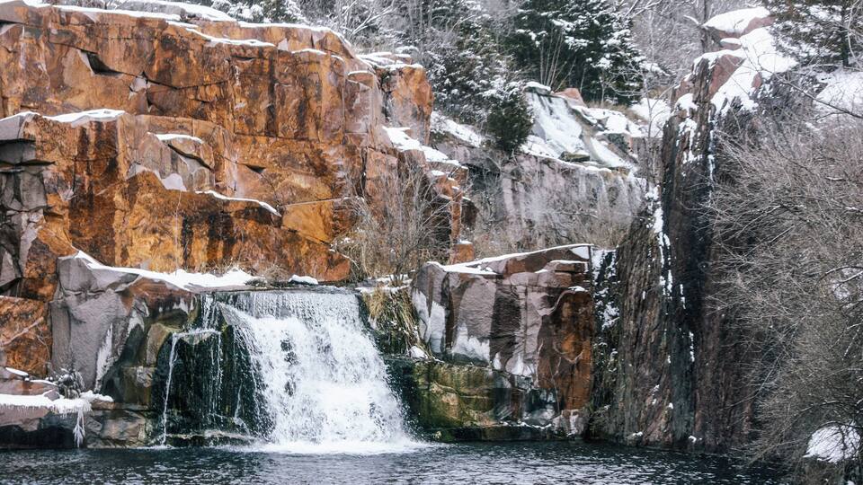A waterfall cascading down a rocky cliff surrounded by snow-covered trees.