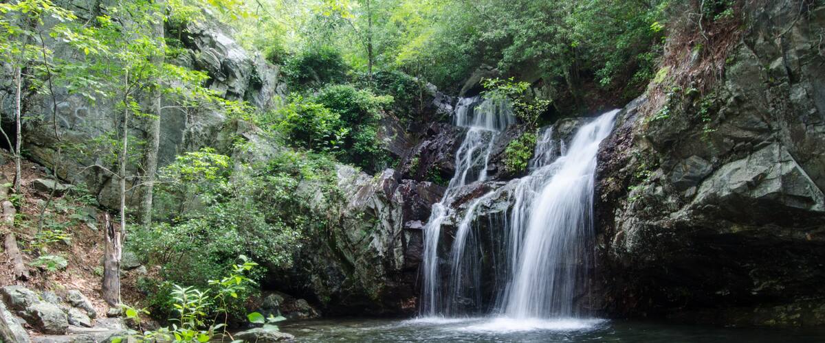 A waterfall cascading into a clear pool surrounded by rocky terrain and lush greenery.