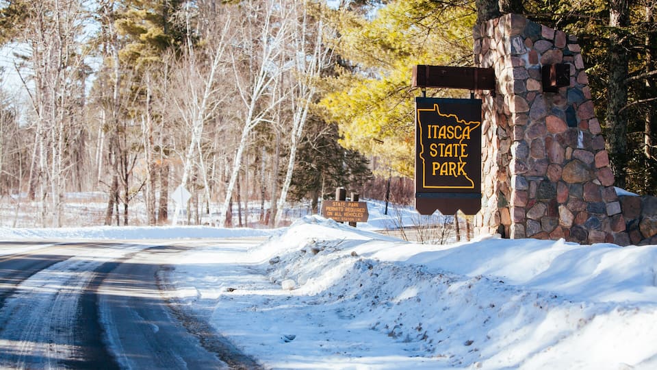 A snow-covered road with a stone wall and a sign indicating Itasca State Park.
