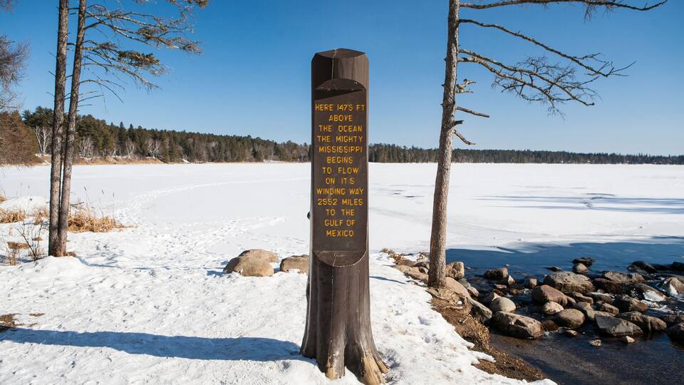A wooden signpost in a snowy landscape with a clear blue sky.