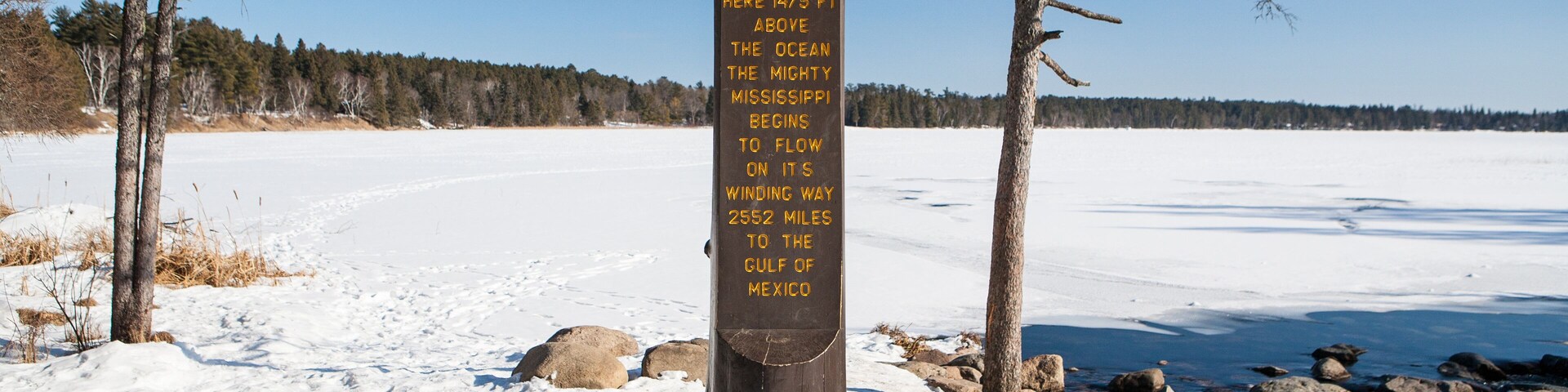 A wooden signpost in a snowy landscape with a clear blue sky.