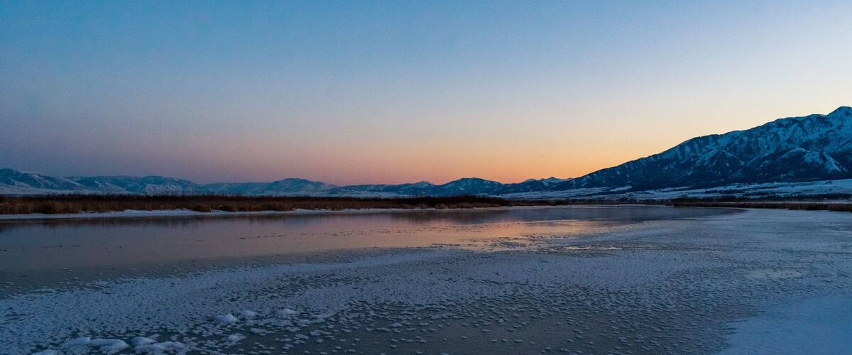 A frozen lake with snow-covered mountains in the background.