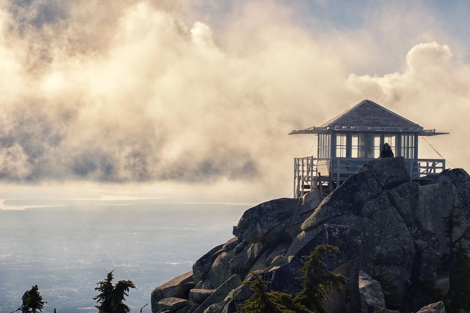 A mountain lookout tower on a rocky outcrop with a view of a valley below.