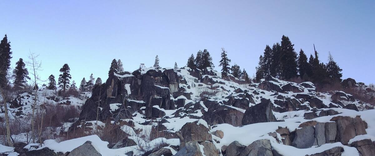 A rocky mountain landscape with snow-covered rocks and sparse trees.