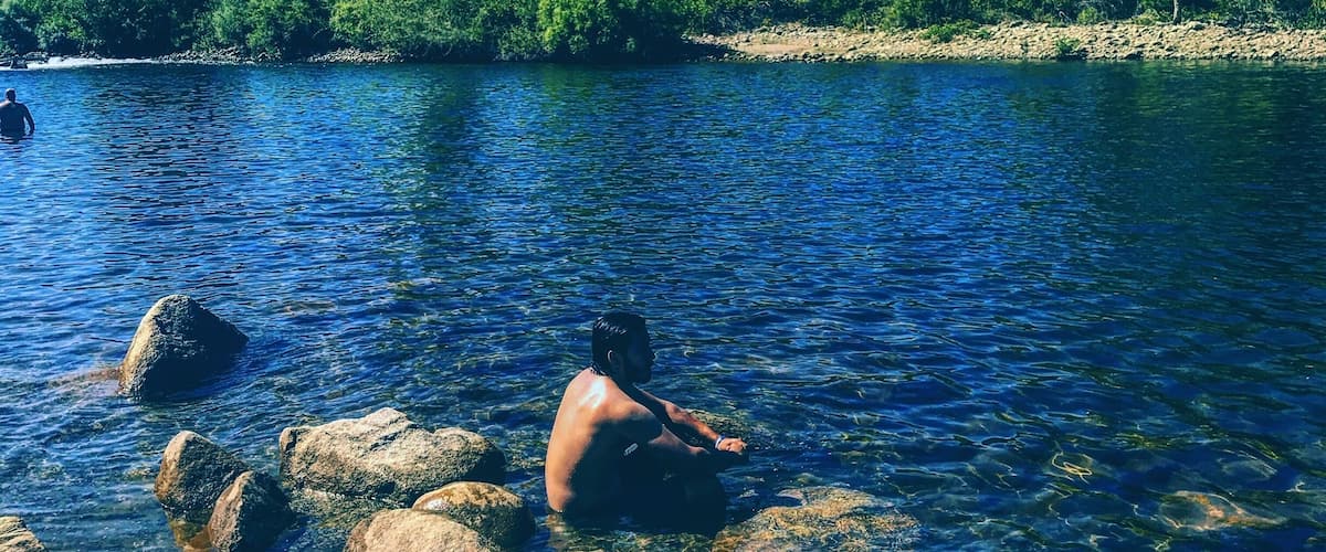 A clear river with rocks and a person sitting on a rock.