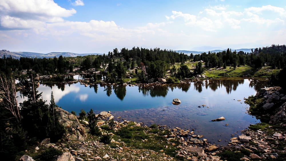 A calm lake surrounded by rocky terrain and dense forest.