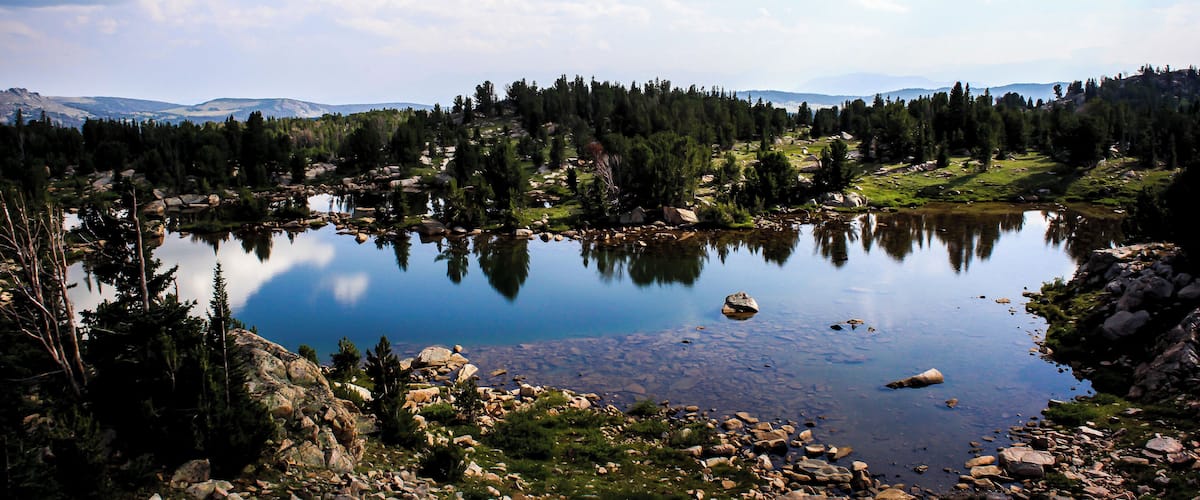 A calm lake surrounded by rocky terrain and dense forest.