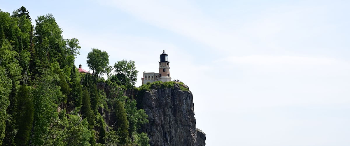 A lighthouse on a cliff surrounded by dense green forest.