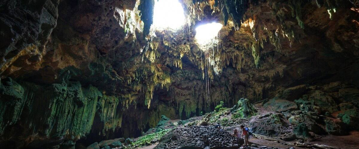A cave with stalactites and stalagmites, a water stream, and people exploring.