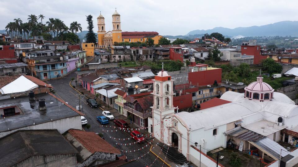 A cityscape with a prominent church with two towers, a mix of colorful buildings, and a mountainous backdrop.