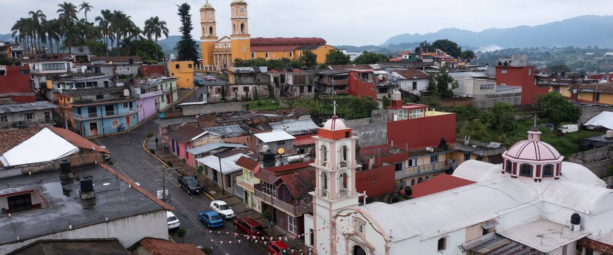 A cityscape with a prominent church with two towers, a mix of colorful buildings, and a mountainous backdrop.