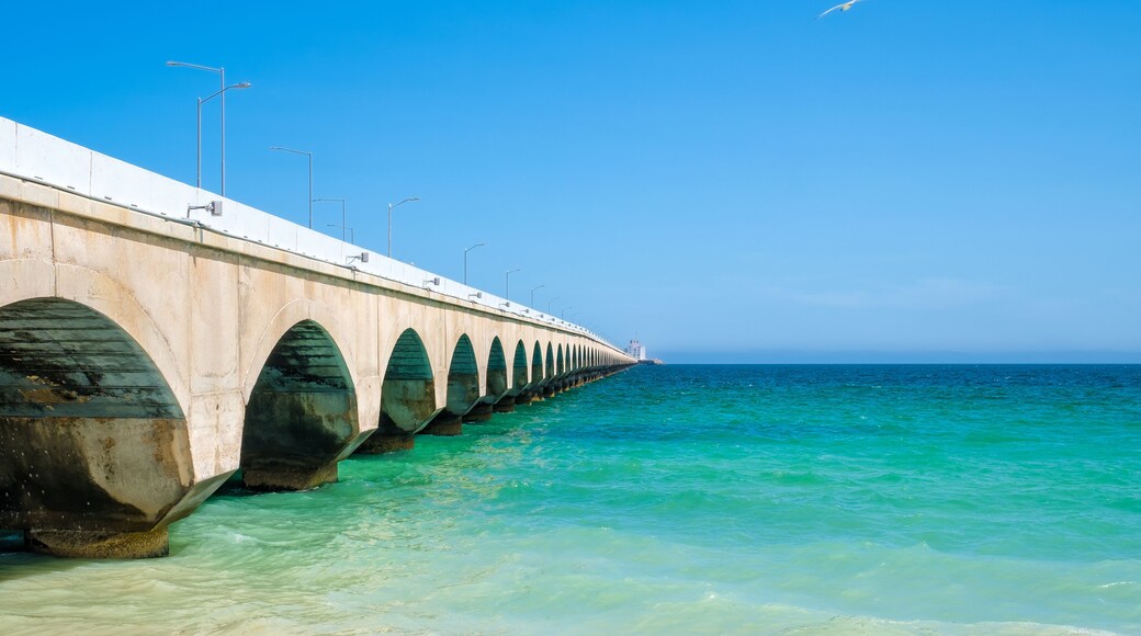 A long pier extending into the ocean with clear turquoise water and a clear blue sky.
