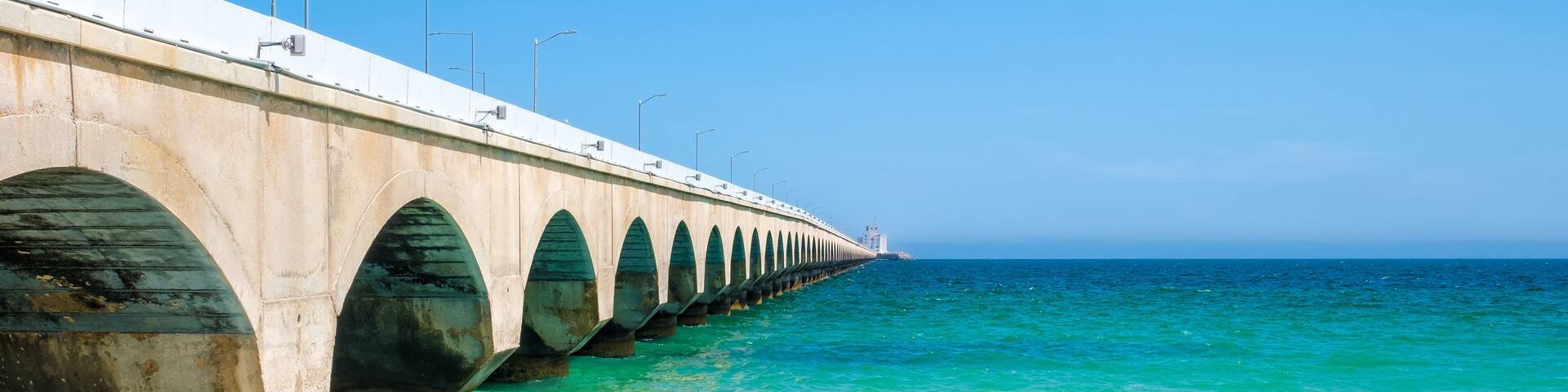 A long pier extending into the ocean with clear turquoise water and a clear blue sky.