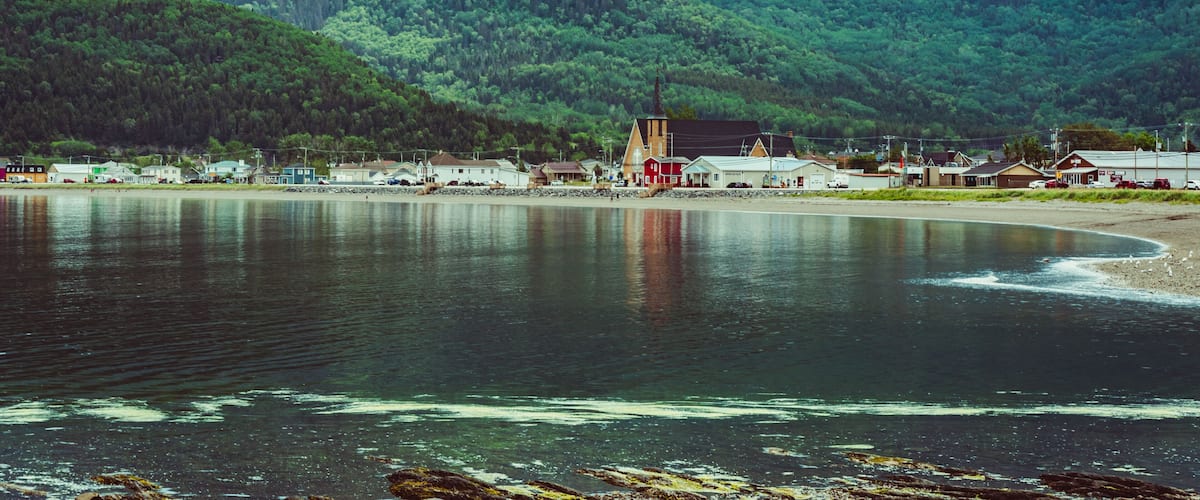 A coastal town with a church, houses, and a forested mountain in the background.