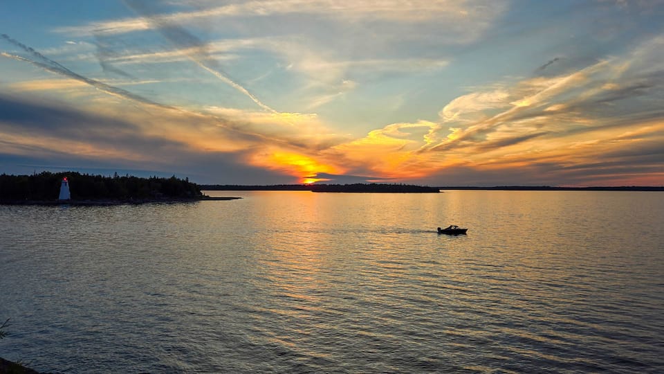 A sunset over a calm body of water with a lighthouse and a small boat.