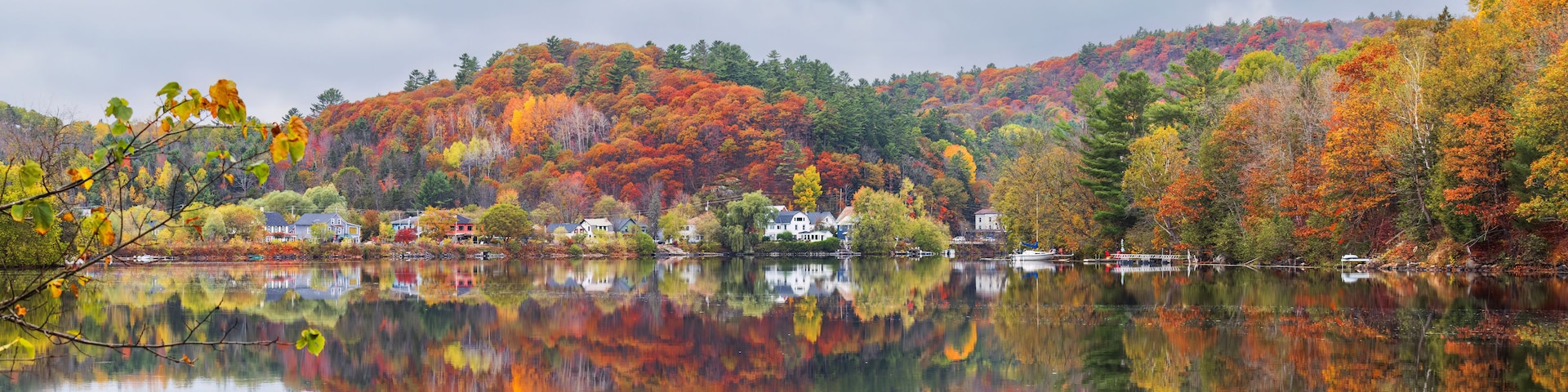 Un lago tranquilo con follaje otoñal reflejado en el agua, rodeado de colinas y casas.