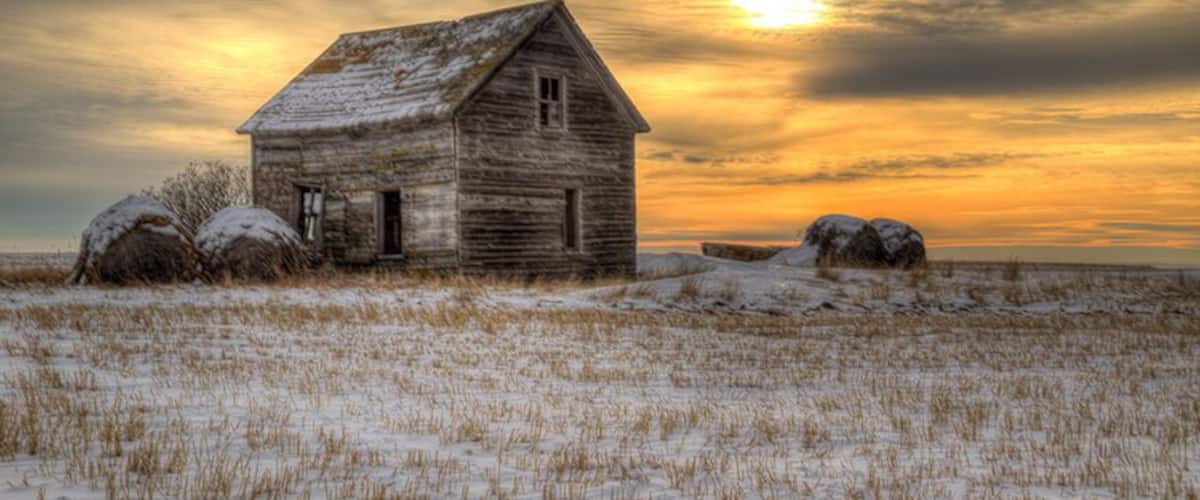 A snow-covered field with a rustic wooden house and large boulders.
