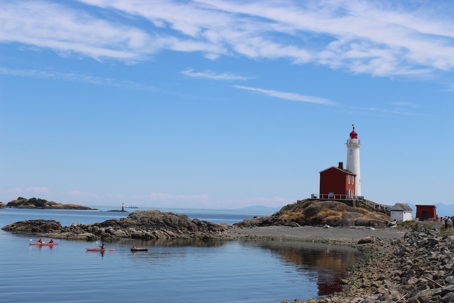 A lighthouse on a rocky island with kayakers in the water.