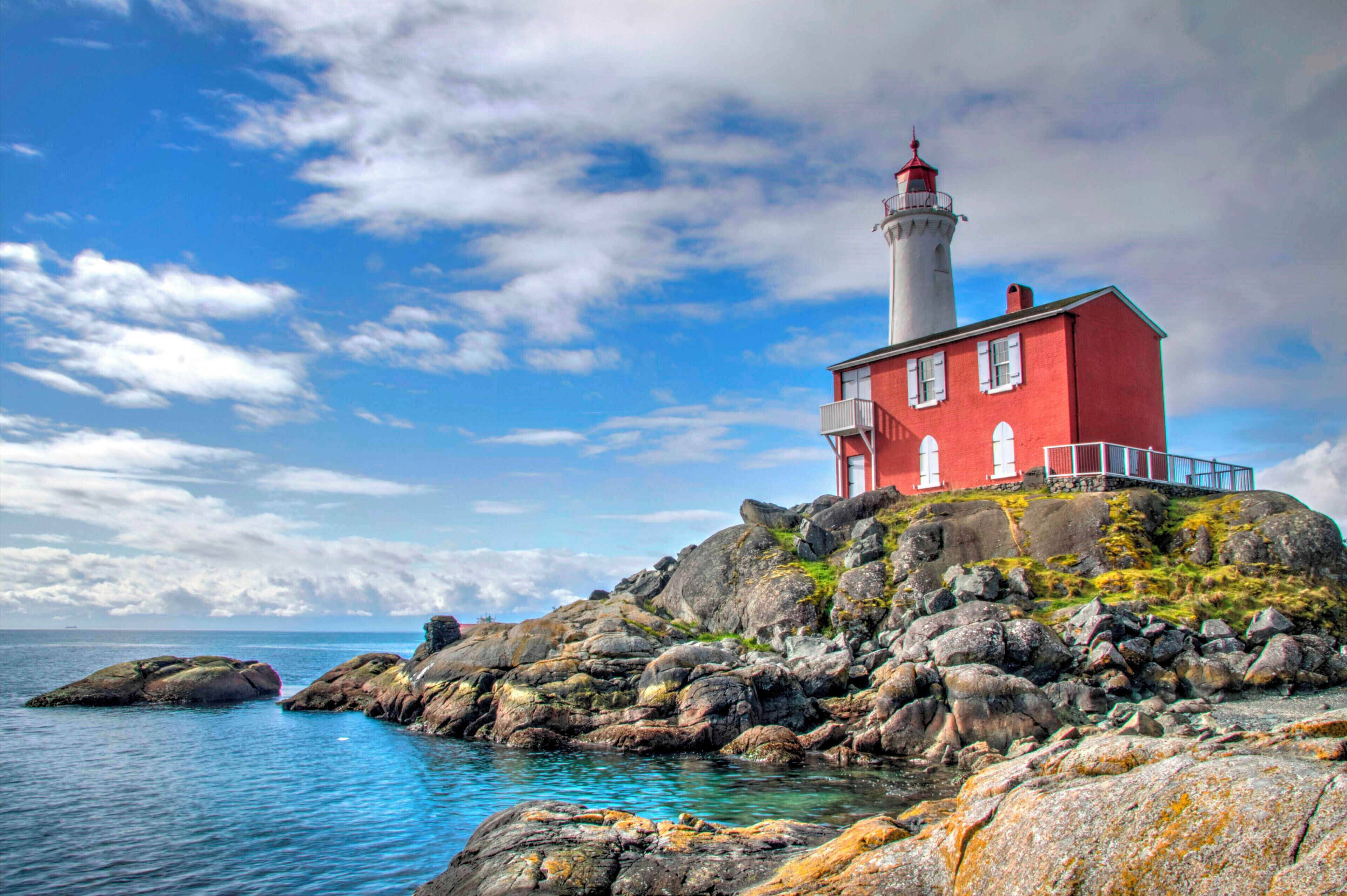 A red lighthouse on a rocky outcrop by the sea.