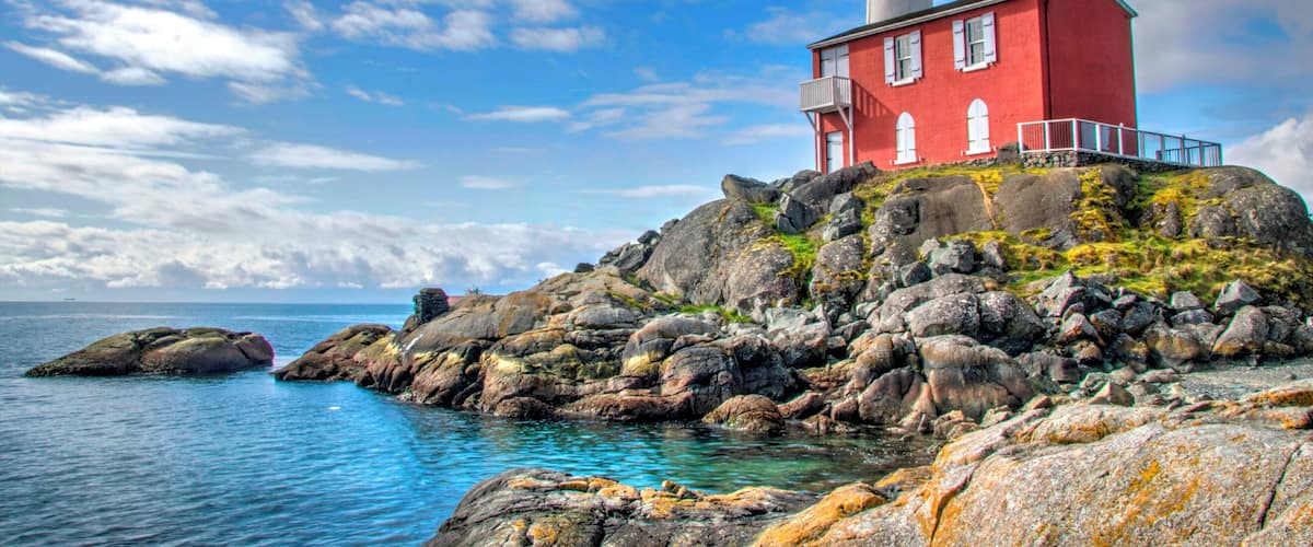 A red lighthouse on a rocky outcrop by the sea.