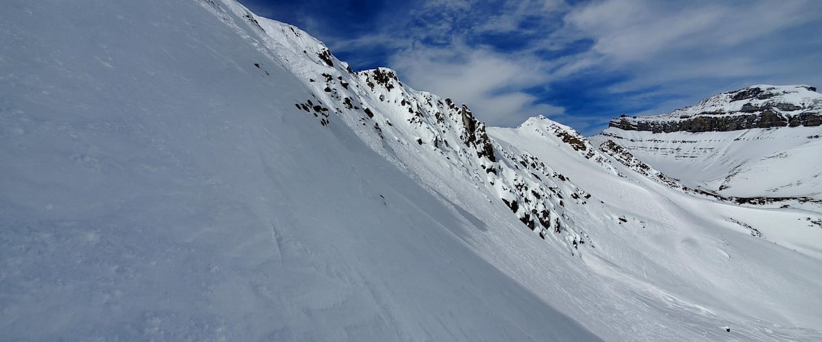 A snow-covered mountain slope with rocky outcrops and a clear blue sky.