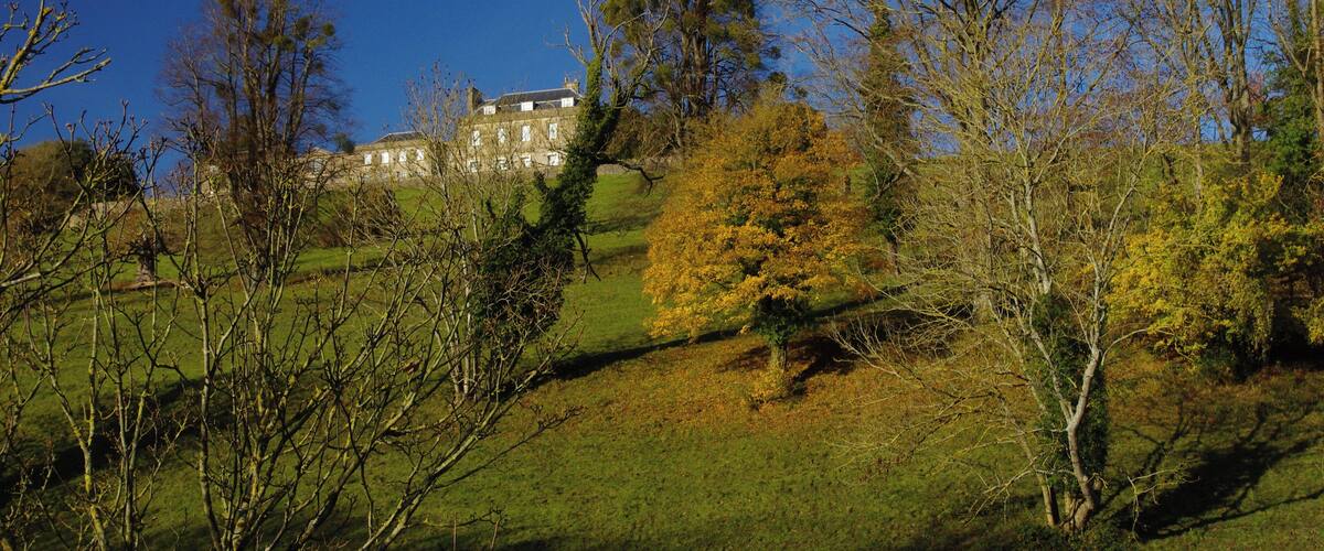 A historic building on a grassy hill with autumn-colored trees.
