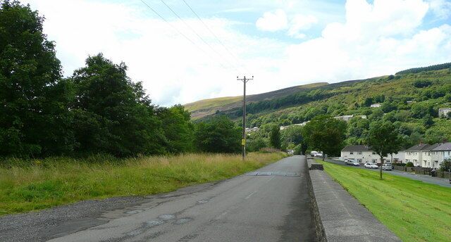 A rural road with houses on one side and a hill in the background.