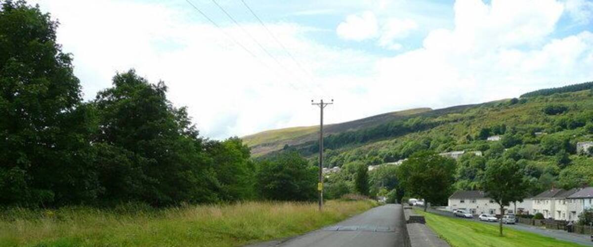 A rural road with houses on one side and a hill in the background.