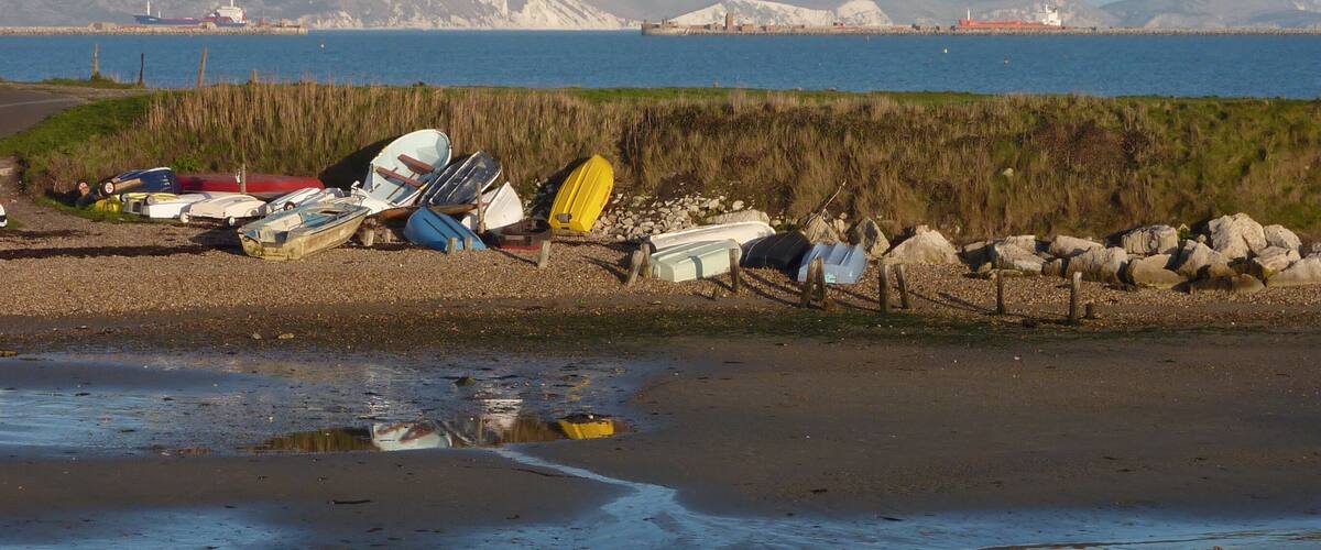 A calm beach with several boats and a lighthouse in the background.