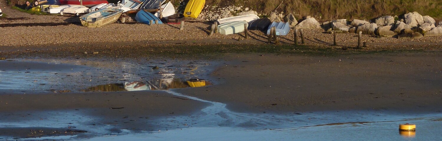 A calm beach with several boats and a lighthouse in the background.