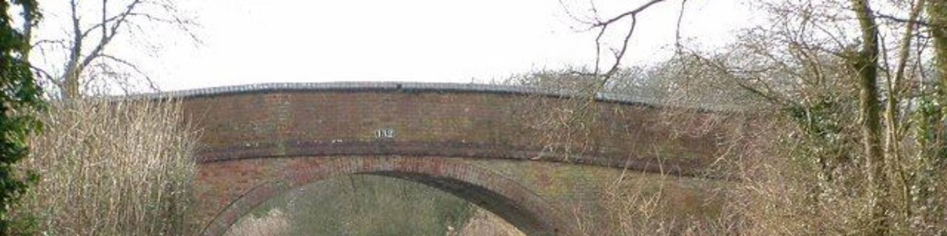 A brick bridge over a calm river with a grassy path beside it.