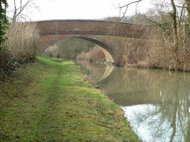 A brick bridge over a calm river with a grassy path beside it.