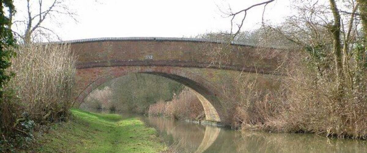 A brick bridge over a calm river with a grassy path beside it.